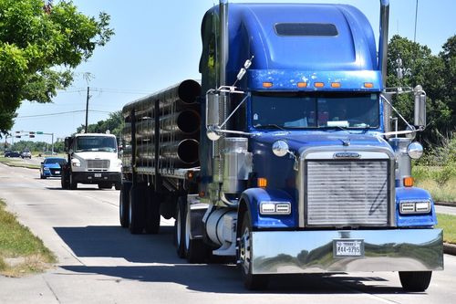 A blue semi truck hauling large pipes on a rural street